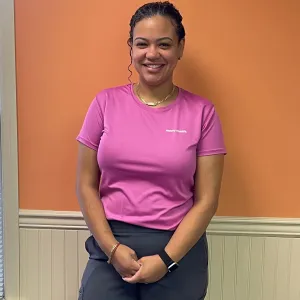 Flor is wearing a pink merry maids tshirt standing in front of an orange and tan wall